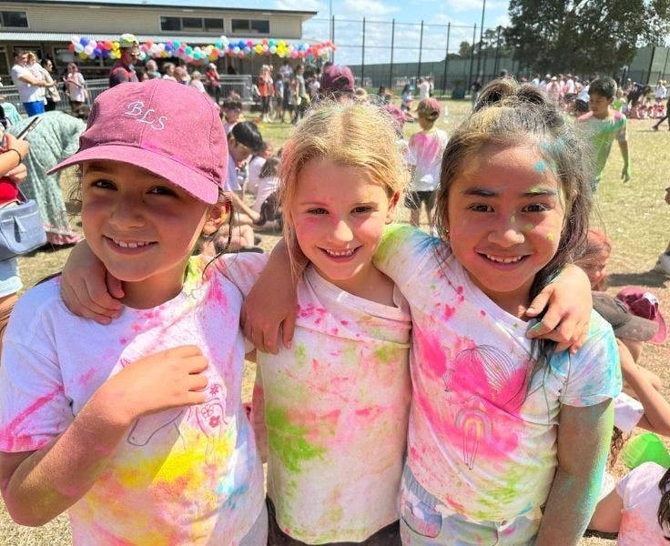 Three students smiling wearing colourful shirts after participating in the colour run