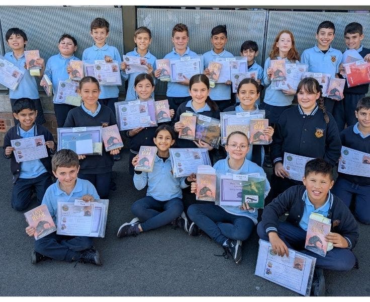 BLSPS Students sitting on the ground displaying a book and certificate