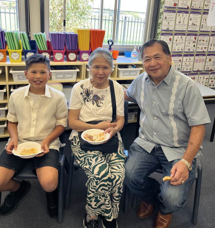 student sitting with his grandparents sharing food in the classroom
